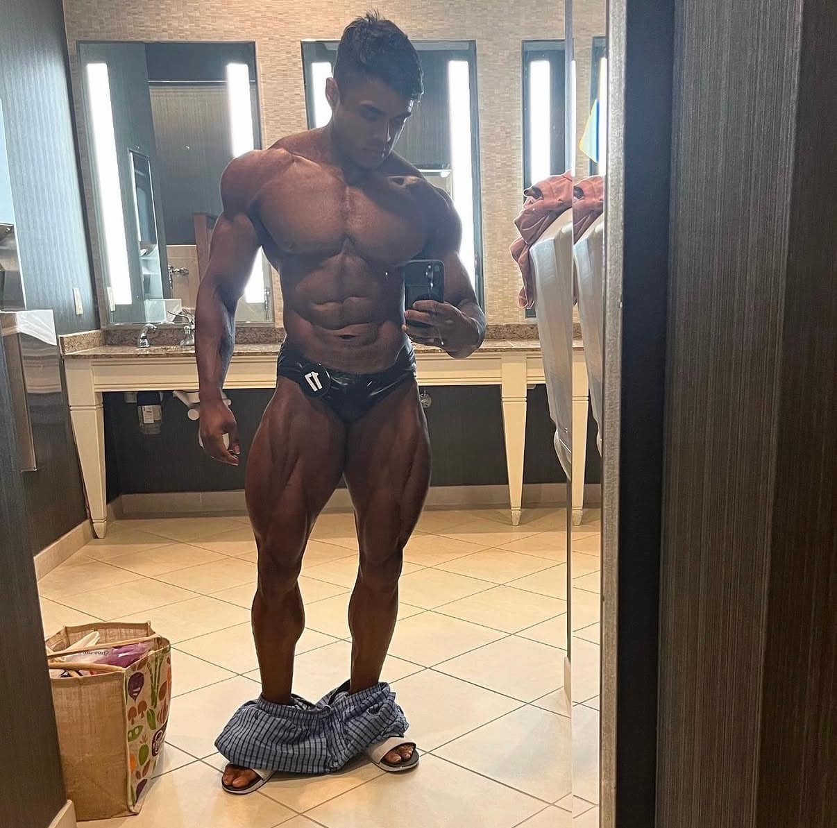 Abe Seth in a deep-tan posing-trunks check-in photo showing an IFBB Pro physique.